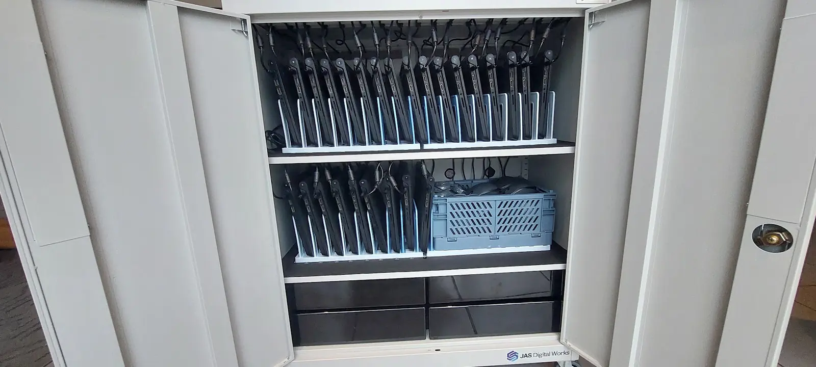 Armoire de stockage et de rechargement ouverte, garnie d'une vingtaine de Chromebooks branchés sur deux étagères.